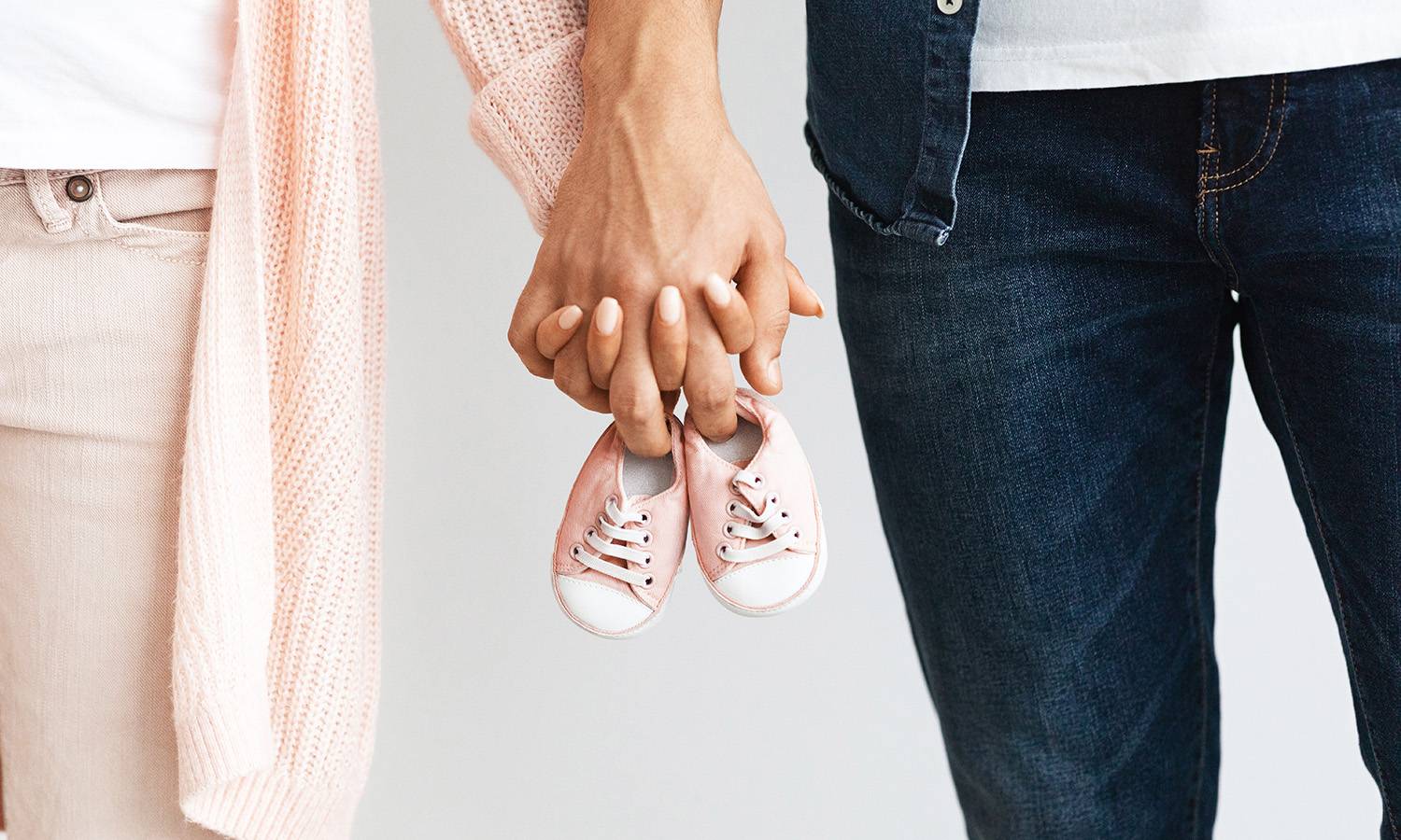 couple holding hands with baby shoes, expecting child from fertility clinic